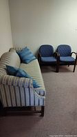 Striped fabric sofa with blue cushions and two blue upholstered armchairs against a white wall