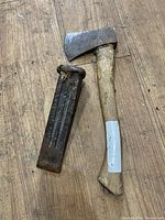 A metal axe head attached to a wooden handle next to a metal wedge placed on a wooden surface.