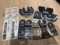 View of 10 cutting blades showing two unopened Tusk jigsaw blade packs and eight assorted used oscillating multi-tool blades of different shapes and brands