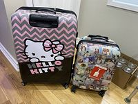 Two hard shell rolling suitcases, one Hello Kitty themed and one with a photo collage design, placed on a hardwood floor corner.