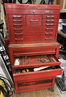 Front view of two-piece red mechanics tool box including top MAC Tools chest and bottom Snap-on chest, some drawers open with miscellaneous items inside