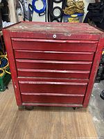 Front view of red metal mechanics tool box with six drawers and visible scratches and wear on paint
