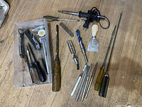 Overview of assorted hand tools including screwdrivers, soldering iron, scraper, and various bits laid out on a wooden surface.
