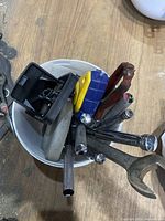 Various metal hand tools, ratchets, sockets, and other tools collected in a container showing wear and rust.