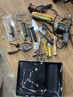 Overhead view of assorted painting and hand tools including paint brushes, scrapers, a brush, and a drill with cord.