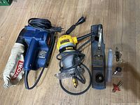 Overview photo showing DEWALT router, Ryobi sander with dust bag, metal hand plane, and multiple router bits on wood floor.