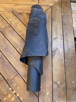 View of tightly rolled black roofing underlayment paper on wooden floor.