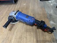 Full view of the Simoniz electric polisher showing the body, side handle, buffing pad, and power cord coiled around the handle.