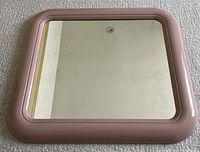 Front view of square mirror showing its rose-colored rounded plastic frame and slightly mottled vintage mirror surface.