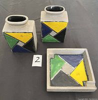 Pair of square vases alongside square tray, showing front colorful geometric glazed panels.