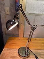 Front angle view showing full height and shape of chrome desk lamp, illuminated light on.