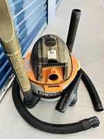 Photo showing the Rigid Shop Vac unit with hoses inserted and resting beside it, condition and basic unit details visible.