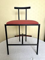 Frontal view showing black tubular frame and rust-red upholstered seat