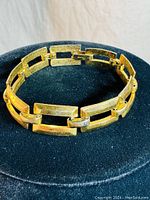 Full view of gold tone vintage CORO bracelet with linked X rectangular shapes on a black display.