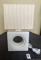 Front view of vintage white Ikea Lovart table lamp showing square ceramic base with circular cutout and rectangular paper shade with vertical lines.