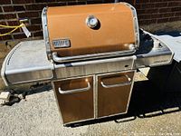 Front view of copper-coloured Weber grill with lid closed showing temperature gauge and side shelves.