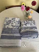 Photo showing folded tablecloth and napkins placed on a round table with fabric texture visible and floral design.