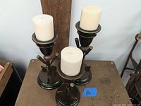 Photo showing three golf themed metal pillar candle stands with off-white pillar candles on top, set on a table with a wooden background and 12-inch ruler for scale.