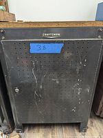 Front view of black Craftsman metal tool cabinet with perforated pegboard door and wooden top.