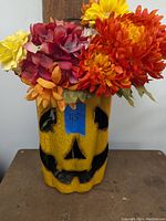 Front view of yellow metal Jack O Lantern with facial cut-outs filled with colorful artificial flowers.