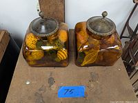 Pair of amber glass jars with antiqued metal lids filled with decorative botanical items