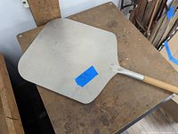 Pizza paddle with a large flat metal surface and short wooden handle on a table.