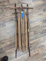 Top down image showing the wooden slats and metal frame of the sled, with a blue tag attached to the center.