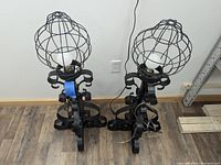 Two tall wrought iron lamps side by side showing curled iron bases and cage-style globe covering bulbs.