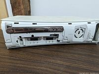 Close-up of Xbox 360 white console front showing disc drive, eject button, and ventilation fan slot.
