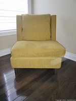 Front view of armless upholstered chair with wood legs and olive-green fabric cushions.