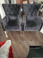 Pair of black upholstered chairs with tufted backs, metal legs, shown from front.
