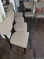Six wood framed dining chairs arranged on hardwood floor showing beige upholstered seats and curved backs.