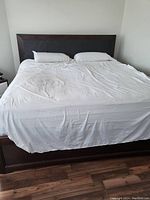 King size bed with white sheet over mattress and dark brown wooden frame with upholstered headboard.