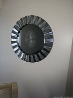Photo of a round mirror mounted on a wall featuring a faceted reflective metal frame with silver tones and a sunburst design.