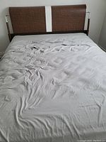 Queen sized bed frame with padded headboard and mattress covered with grey bed sheet.