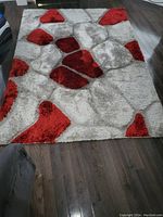 Top-down view of the rectangular stone pattern area rug on a dark hardwood floor showing grey and red color design.