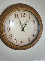 Front view of round wall clock with brown wooden frame, cracked glass face, and ornate black clock hands.