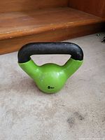 Green 5-pound kettlebell weight with a black handle placed on a carpeted surface.