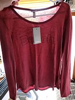 Front view of burgundy long sleeve Bench shirt on hanger, showing logo and tag.