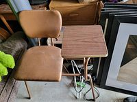 Photo showing side view of brown vinyl chair with metal legs and attached rectangular side table with wood-like laminate top.