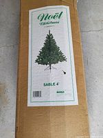 Cardboard box packaging showing a printed label with Noël Christmas branding, depicting a green artificial Christmas tree labeled 'Sable 4'.