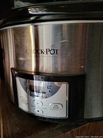 Close-up of the Crock-Pot logo and digital control panel with bilingual buttons and slight surface scratches.