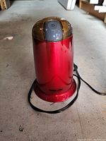 Red metallic electric food chopper with power button on lid and attached cord, placed on floor.