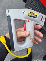 Photo of Stanley SharpShooter T801 electric stapler held by hand, showing overall stapler design, label, trigger, and power cord.