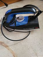 Side view showing the iron's black and blue body, dial, and brand label.