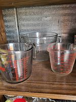 Photo shows three glass measuring cups with volume measurement markings in milliliters and cups. Cups have handles and pouring spouts.