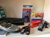 Image showing a Brother label maker, stapler, scissors, hole punch in packaging, index cards and tape dispenser.