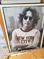 Framed black and white photograph of John Lennon with sunglasses and New York City t-shirt, slightly angled.