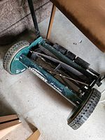 Side angle view showing green metal body, black rubber tread wheels, visible blade reel and some wear.