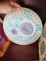 Front view of a round stone decorative plaque featuring detailed sunflower and leaves design with green paint accents.